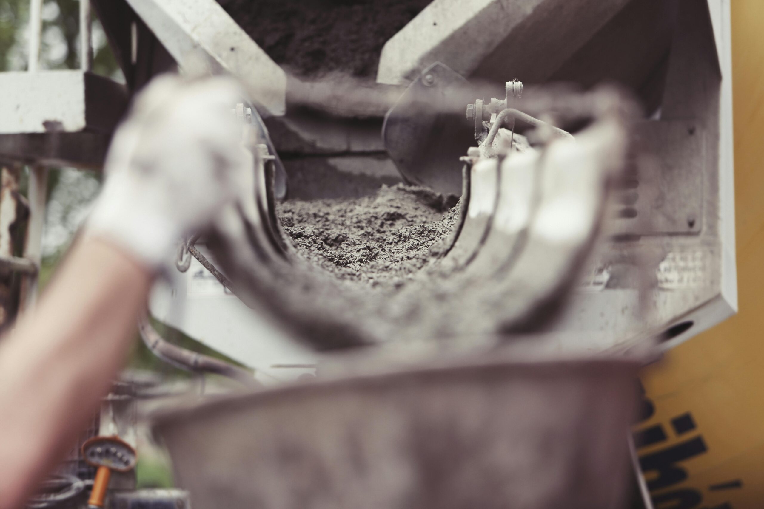 Close-up of concrete being poured from a mixer truck at a construction site with a worker's hand visible.