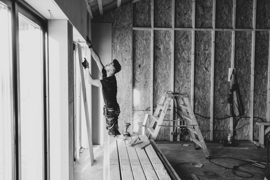 Black and white photo of a worker installing drywall indoors, Falun, Sweden.